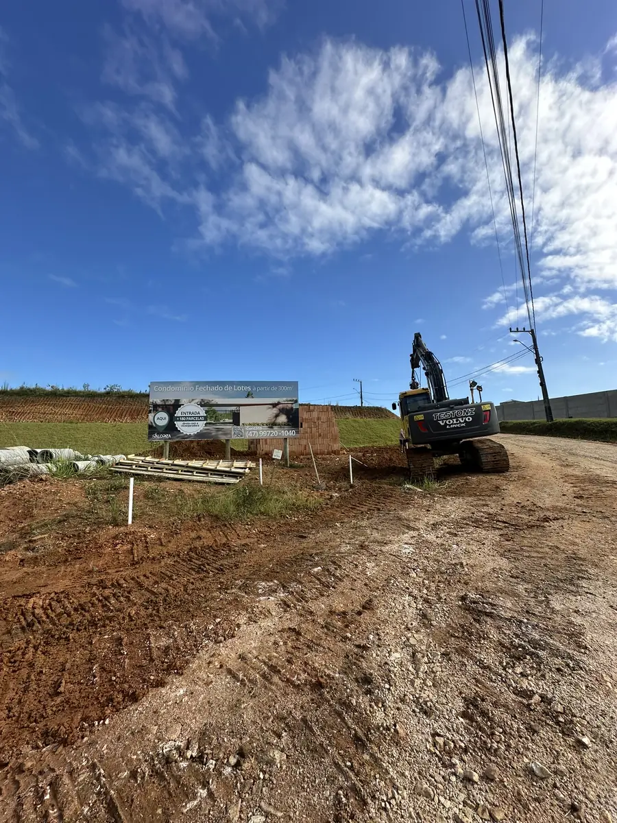 Escavadeira trabalhando no acesso principal, ao lado do letreiro de obra do condomínio