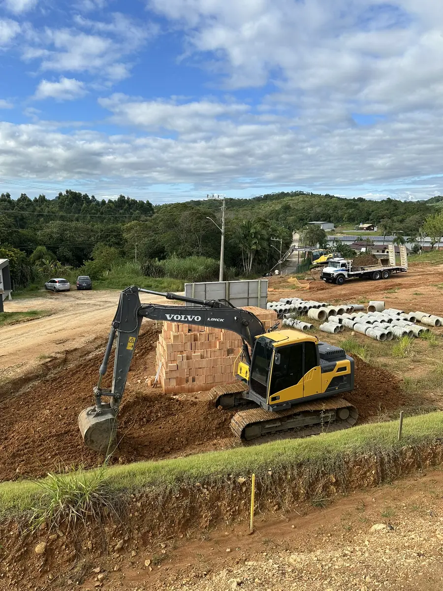 Muro de tijolo da portaria erguido, com escavadeira e aduelas de concreto ao lado