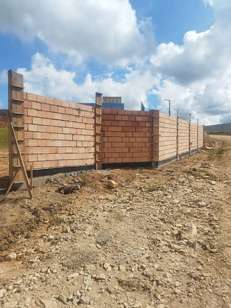 Muro de tijolo maciço fechando a divisa, com a placa indicando o acesso aos lotes